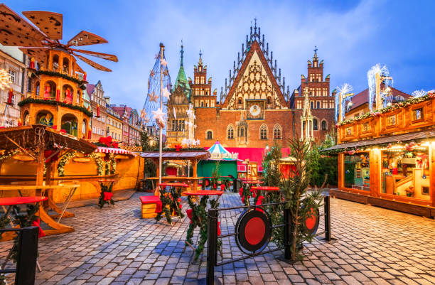 A festive European Christmas market at dusk, with wooden stalls on a cobblestone square before historic buildings.