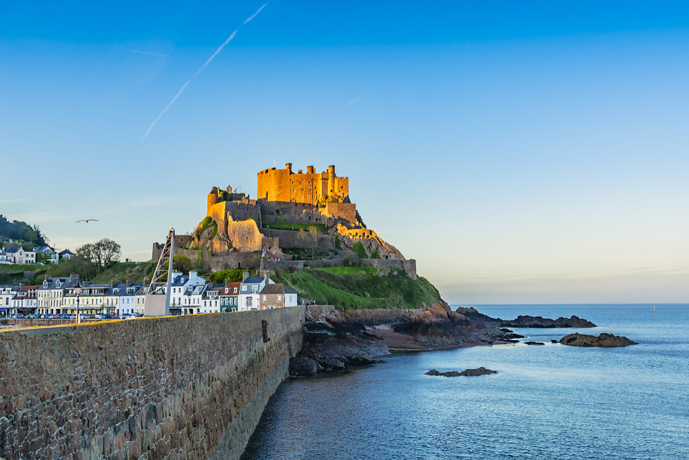 A castle on a hill overlooking a coastal town and the sea, illuminated by golden light.