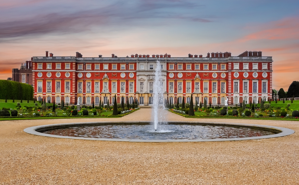 A grand, red-brick palace with a large fountain and manicured gardens in the foreground.