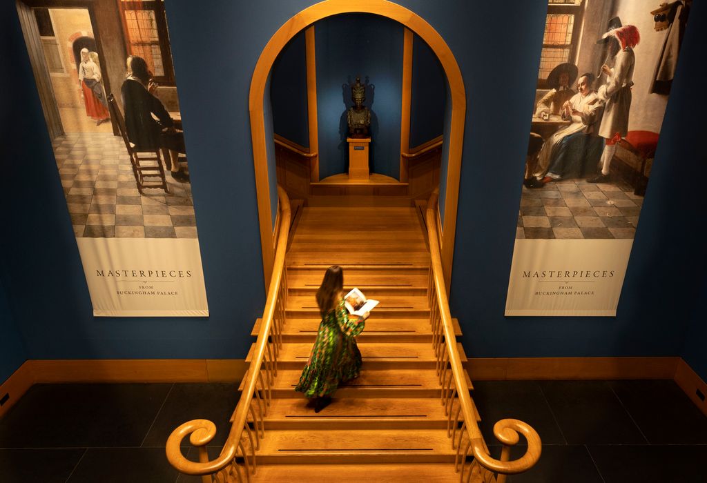 A high-angle view of a woman walking up a grand wooden staircase in an art gallery.