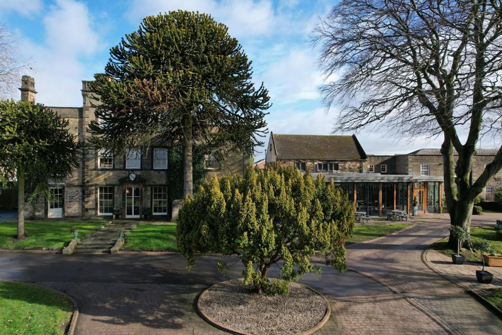 A large stone country house with a circular driveway and mature trees on a partly cloudy day.