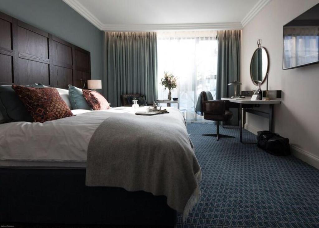 A hotel room with a bed, a desk and chair, and a large window with blue curtains.