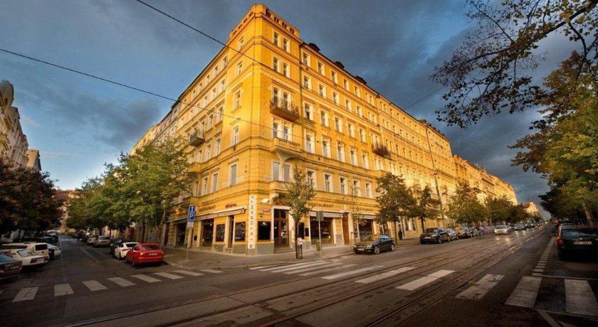 A large, yellow corner building on a city street with tram tracks, cars, and trees.