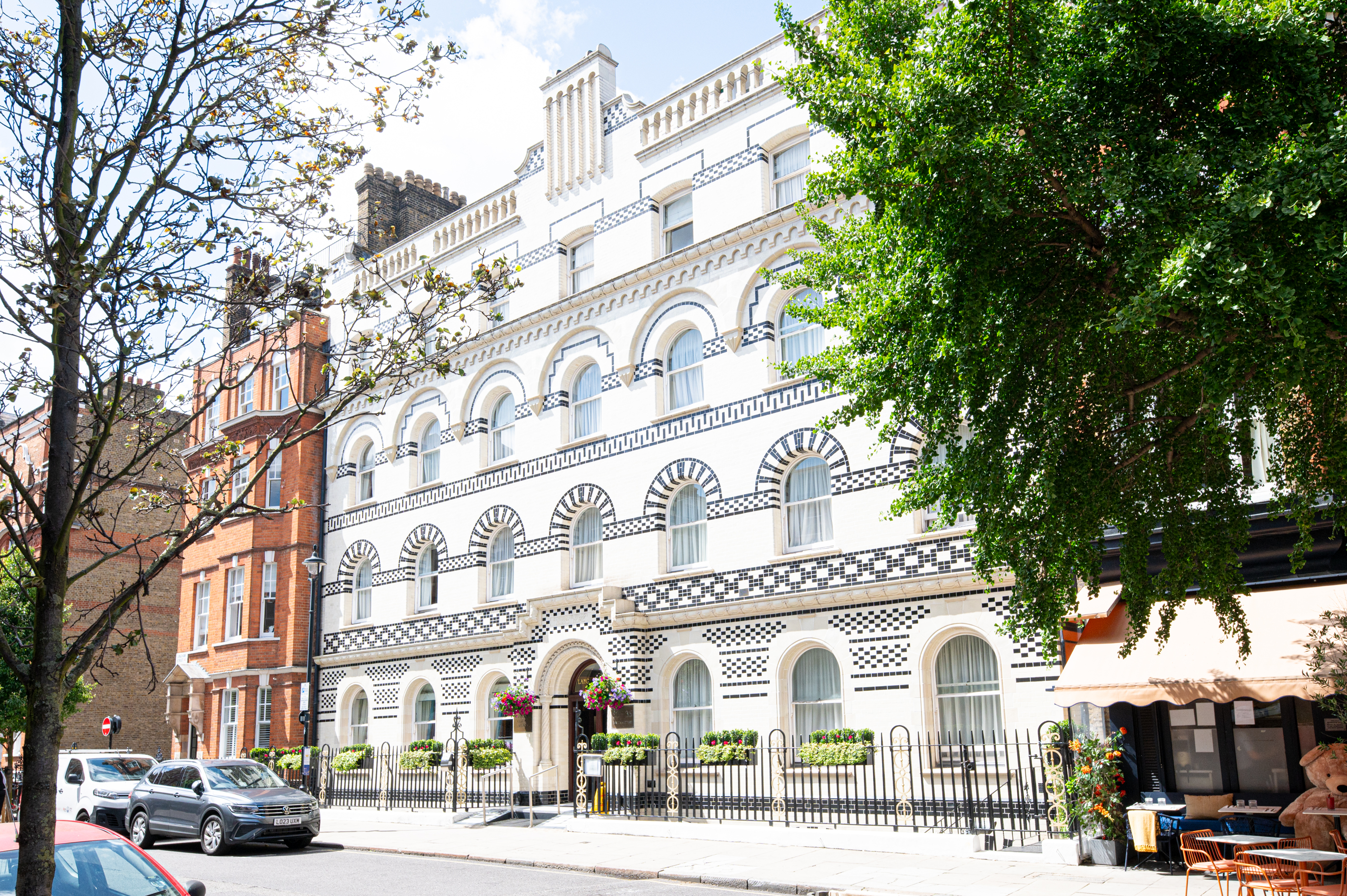 The ornate white and black facade of a building on a sunny, tree-lined city street.