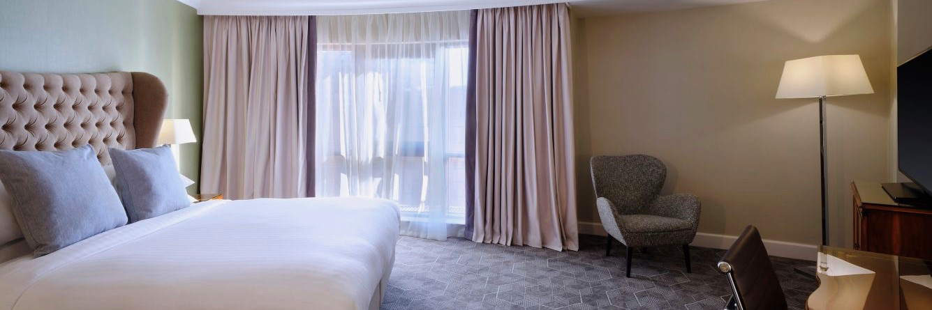 A nicely appointed hotel room with a large bed next to a window, and an armchair in the corner.