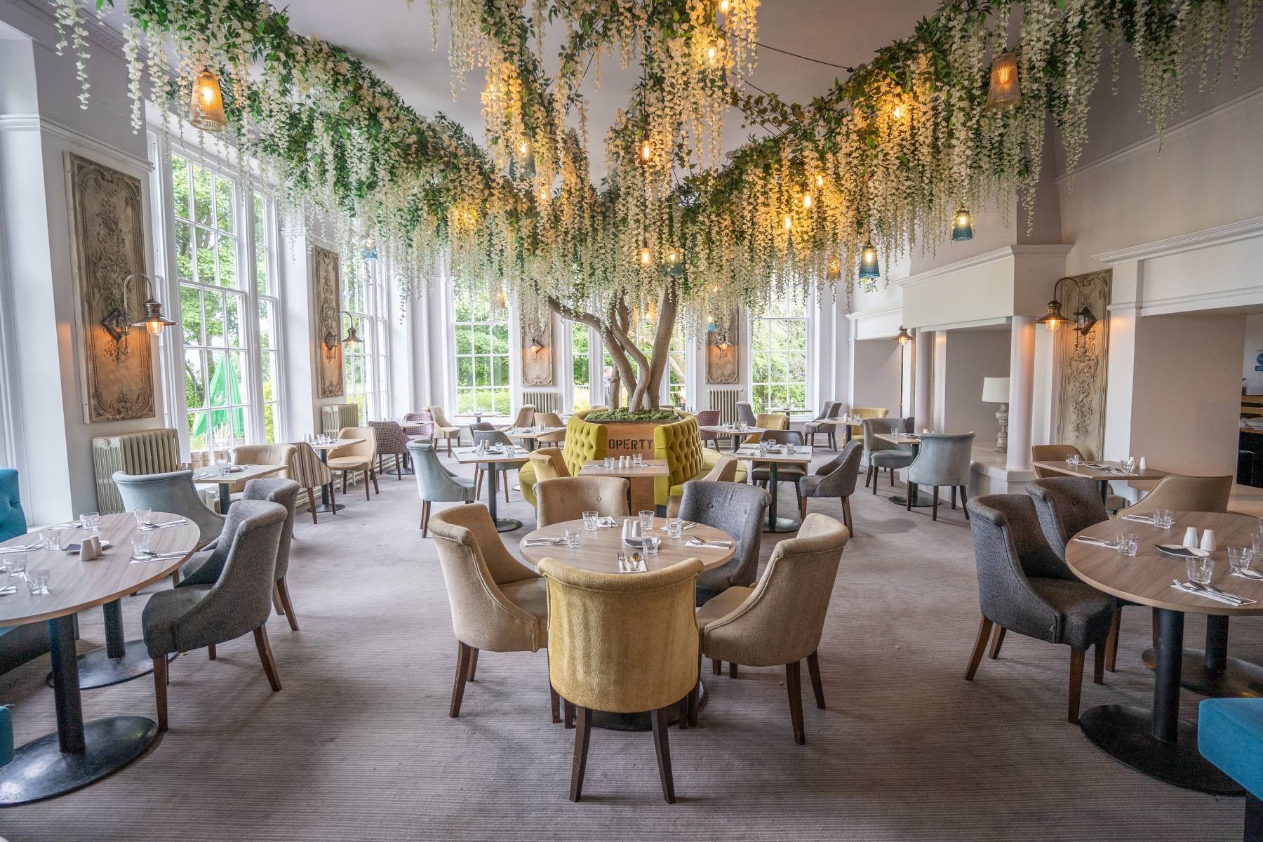 A restaurant dining room with tables set under an elaborate ceiling decoration of hanging white flowers and lights.