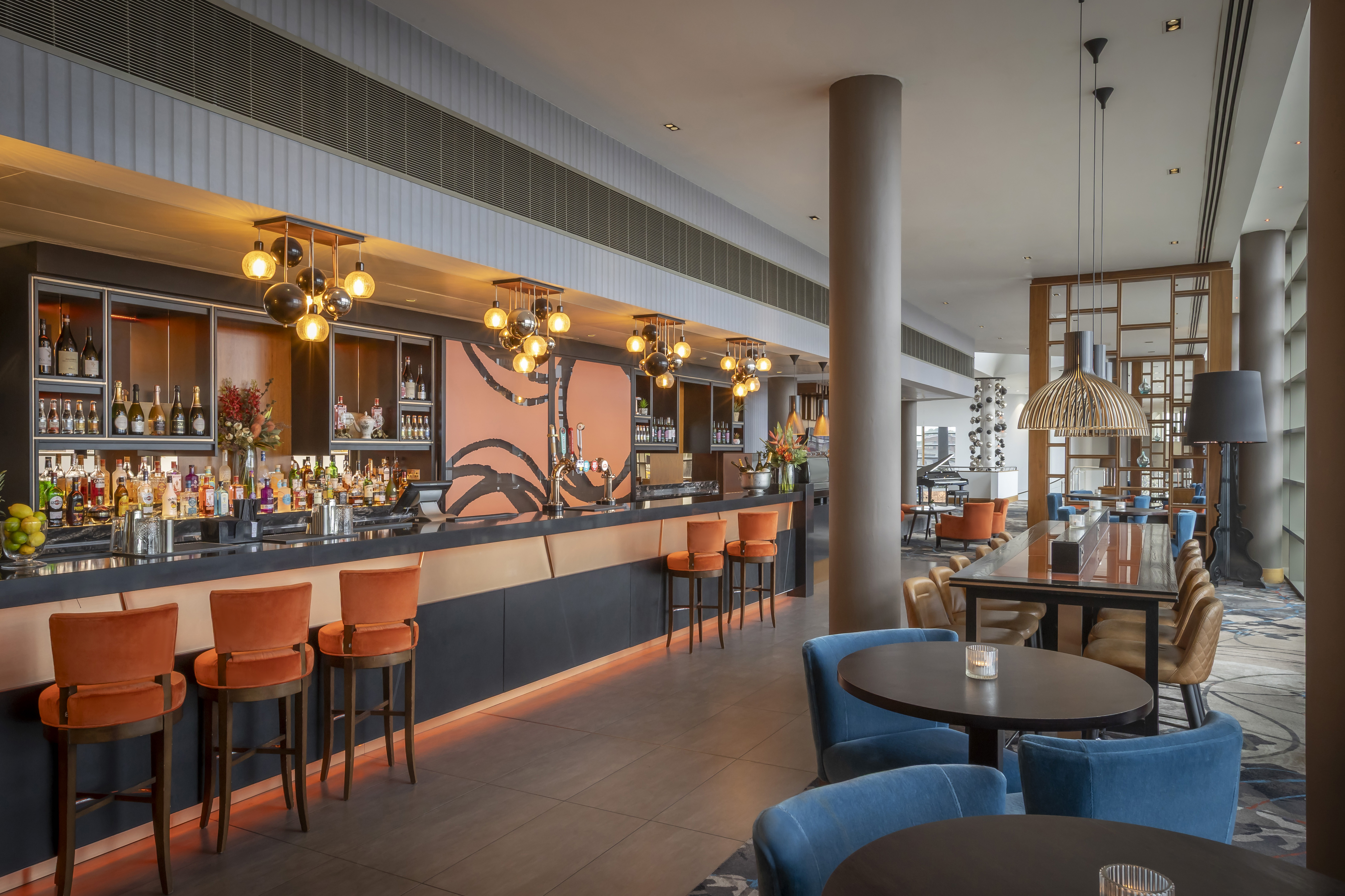 The interior of a modern, empty hotel bar and lounge with colorful velvet seating and contemporary lighting.