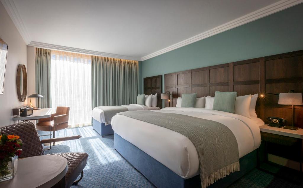 A spacious hotel room with two beds, a seating area, and a large window with long curtains.