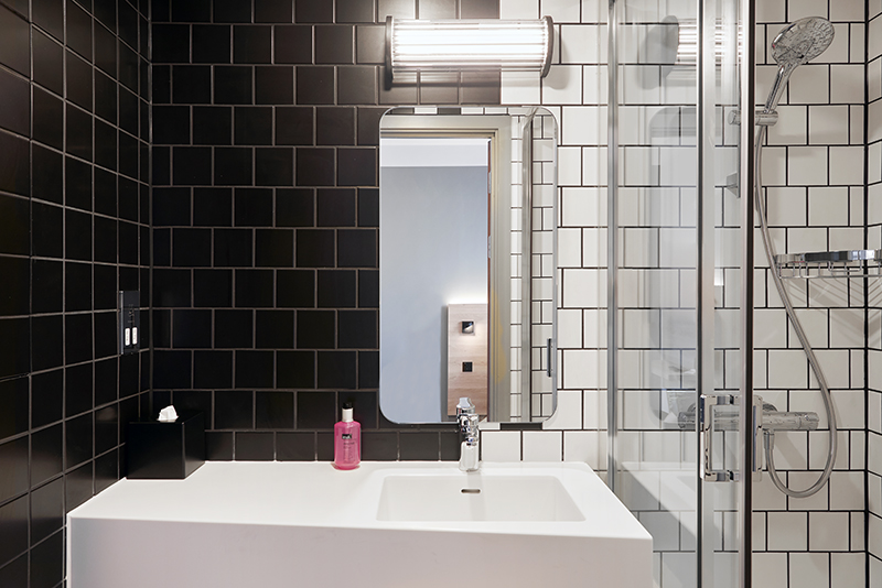 A modern bathroom with a white sink against a black tiled wall, next to a white-tiled shower.
