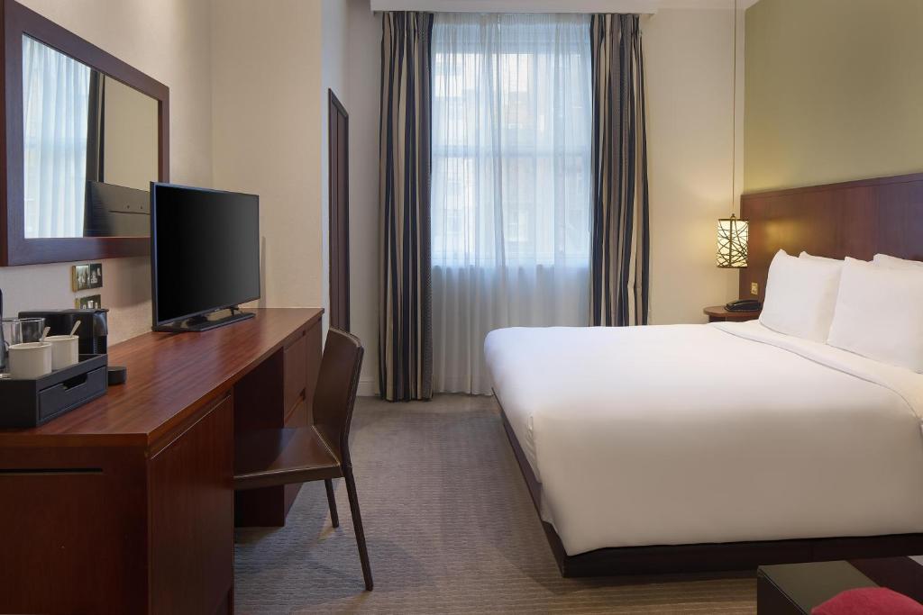 A hotel room with a large bed, a desk with a television, a chair, and a window.