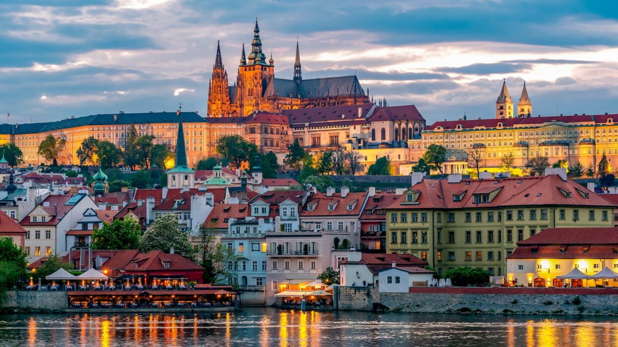 The illuminated Prague Castle complex overlooking the city and a river at dusk.