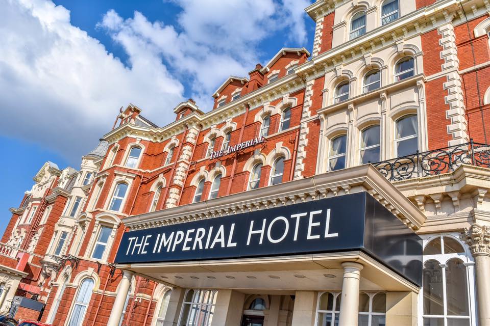 A low-angle shot of the ornate, red-brick facade of The Imperial Hotel against a blue sky.