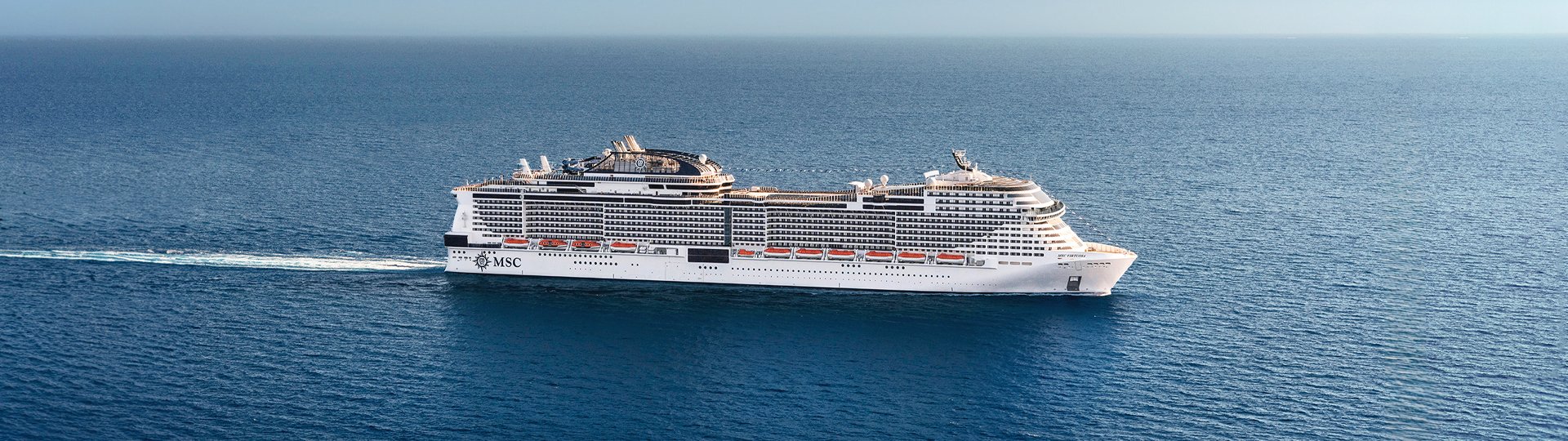 An aerial view of a large, white MSC cruise ship sailing on the open blue ocean.