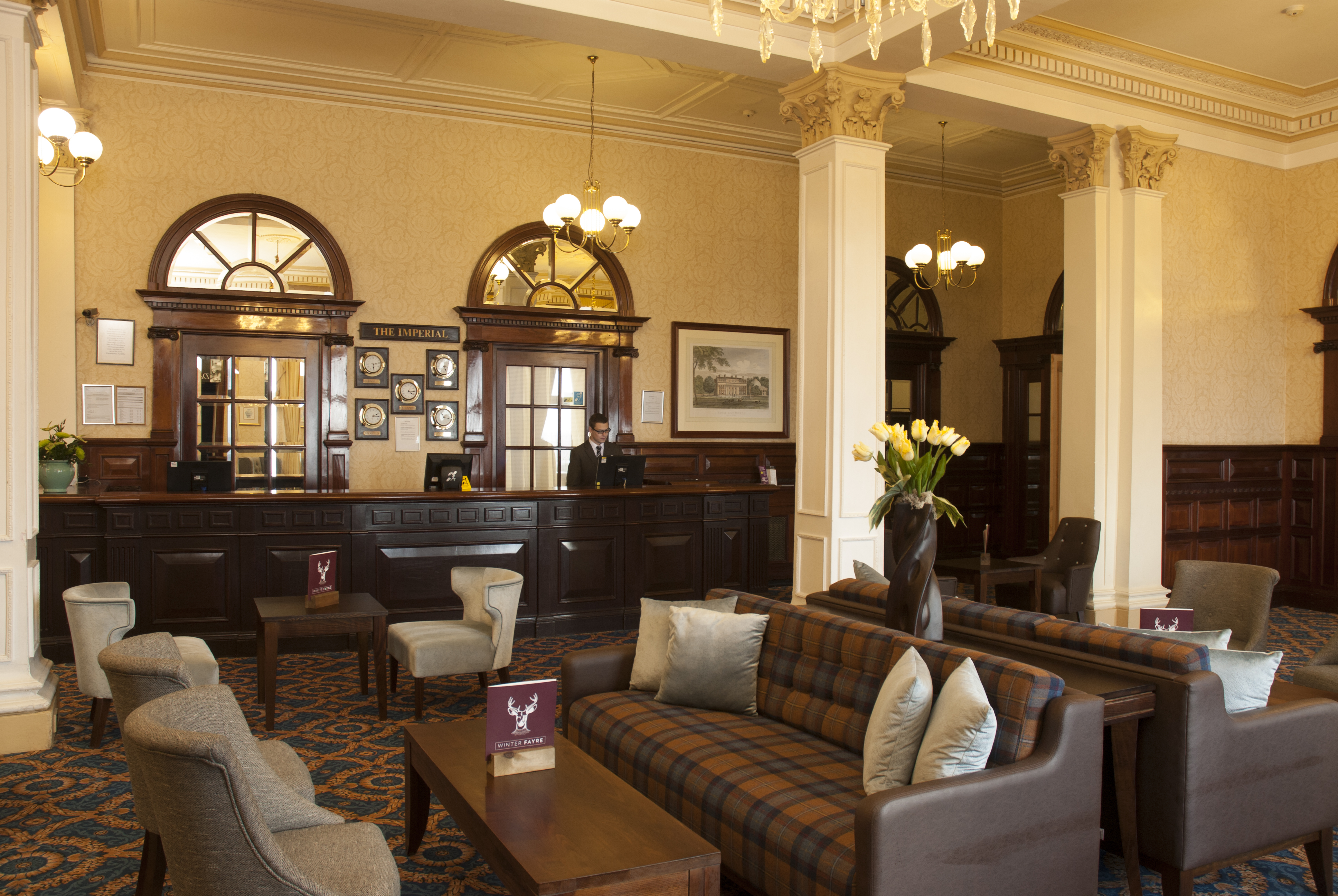 The ornate lobby of The Imperial hotel, with a reception desk and a seating area with plaid sofas.