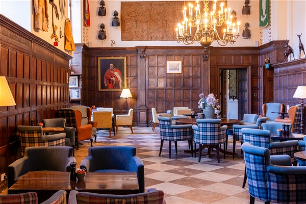 A grand, wood-paneled lounge with plaid armchairs, a checkered floor, and an ornate chandelier.