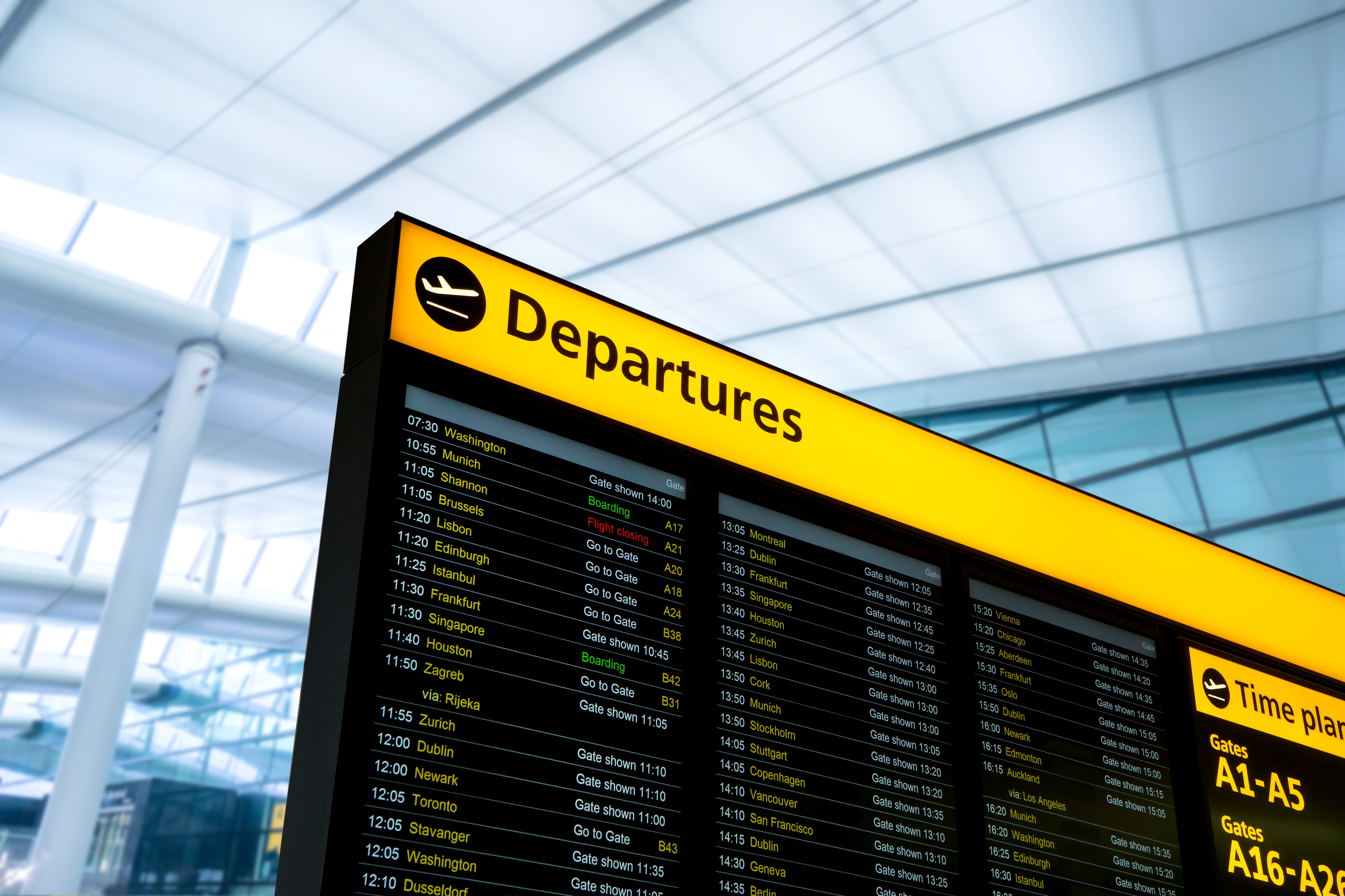 A close-up of a bright yellow airport departures board displaying flight times and destinations.