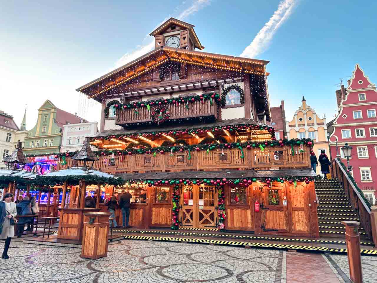 A large wooden building decorated with Christmas lights and garlands in a cobblestone town square.