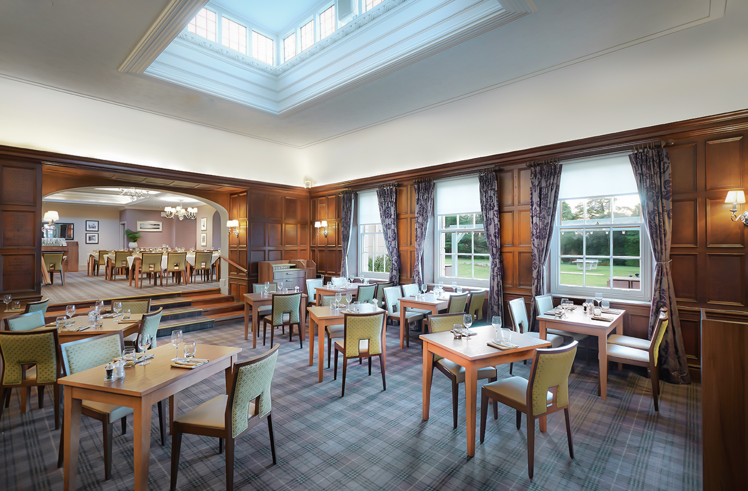 An upscale restaurant dining room with wood-paneled walls, plaid carpet, and tables set for service.
