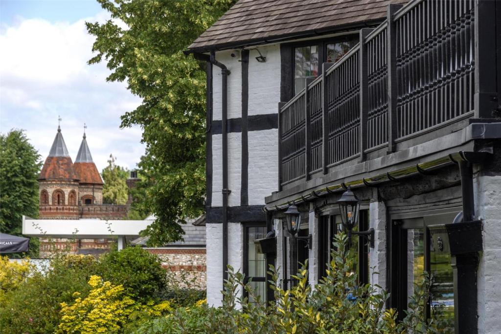 A white and black half-timbered building with a balcony, with two brick towers visible in the background.