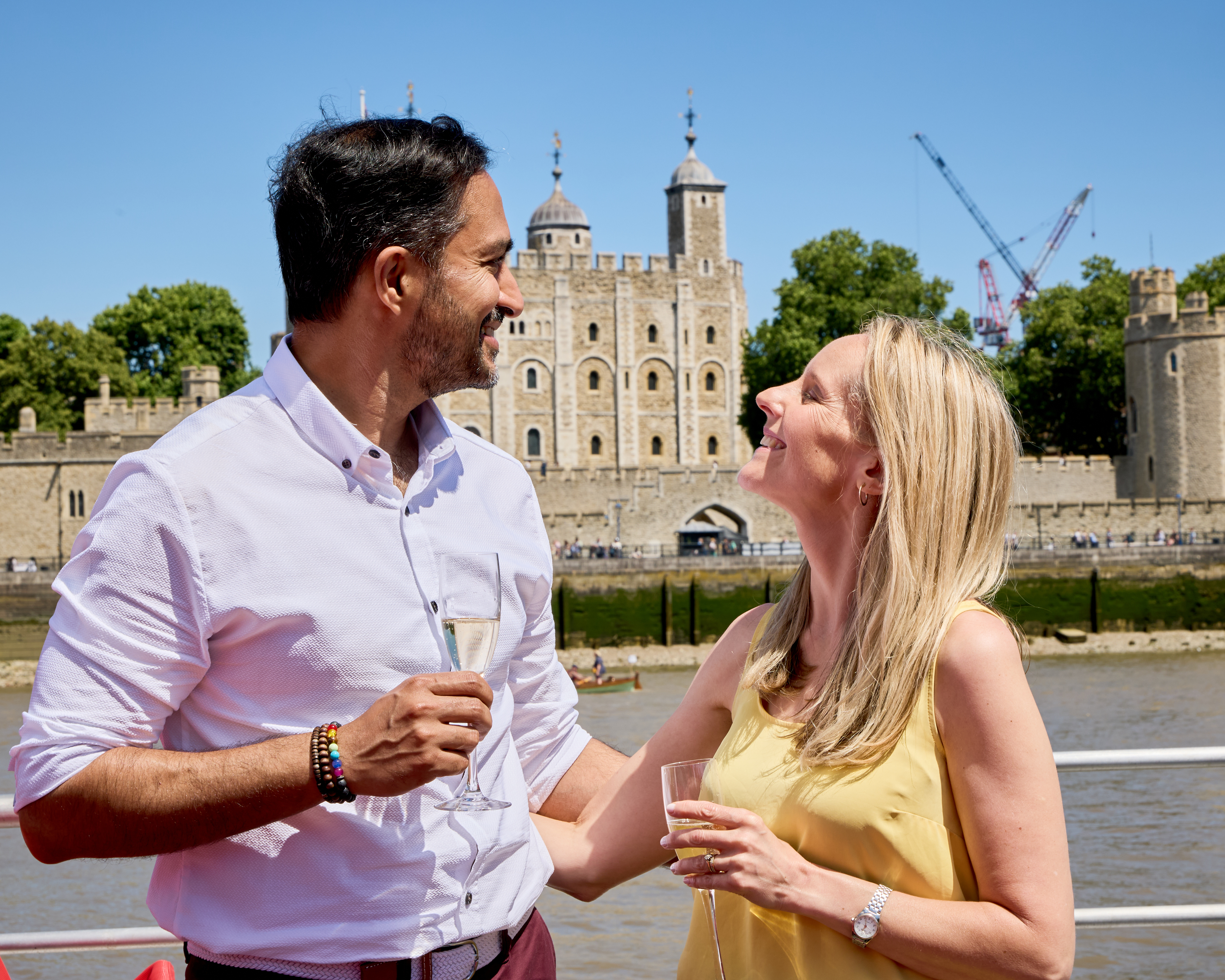 A man and woman smile at each other holding champagne with the Tower of London in the background.