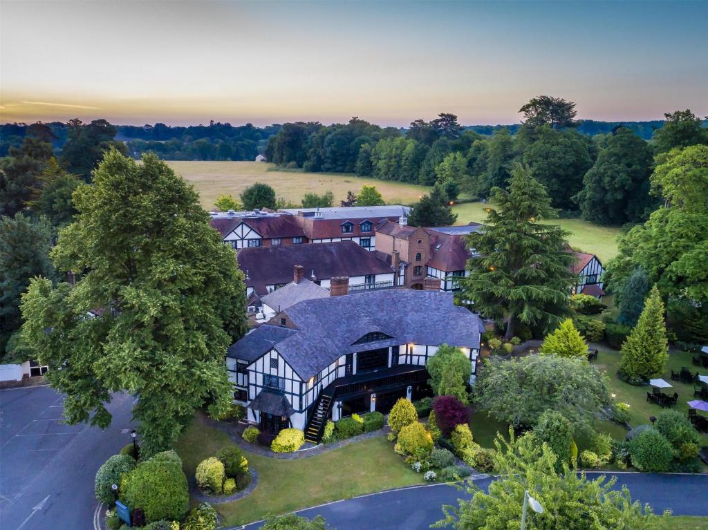 An aerial view of a large Tudor-style building complex surrounded by lush trees and fields at dusk.
