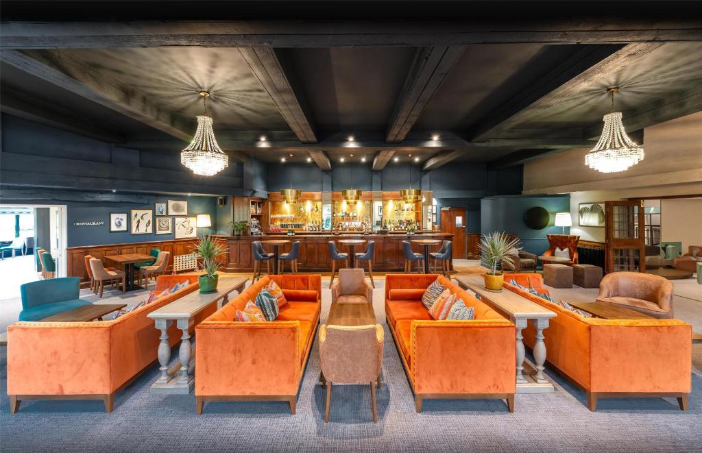 The interior of a stylish bar and lounge with orange sofas, a dark ceiling, and a wooden bar.