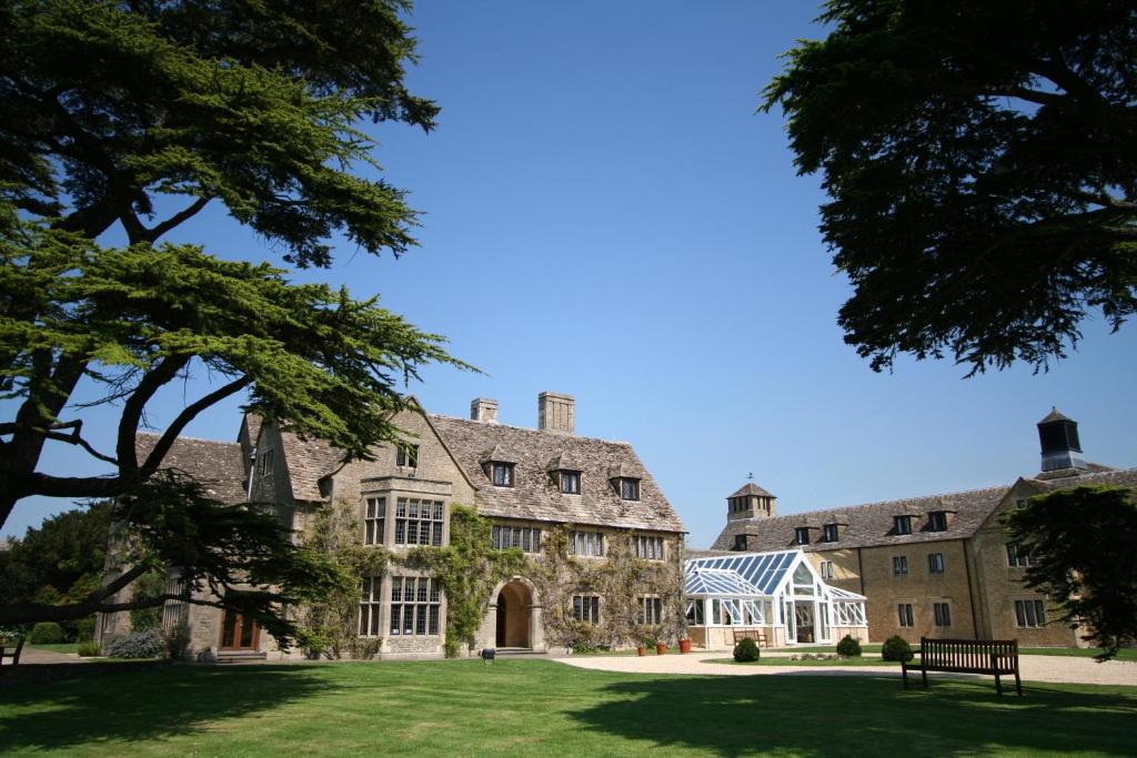 A large, stone country manor with a green lawn and trees, under a clear blue sky.