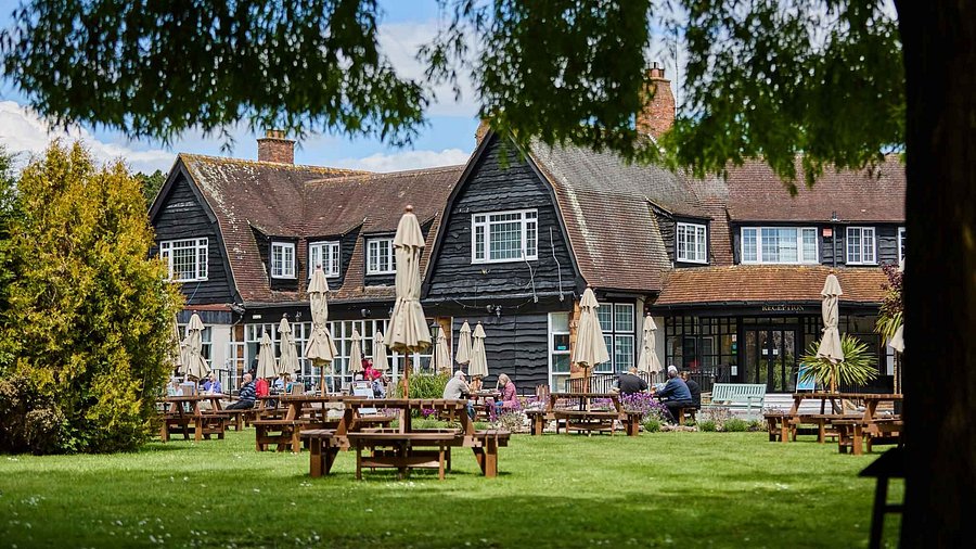 A large, dark-sided inn with people sitting at picnic tables on a spacious green lawn.