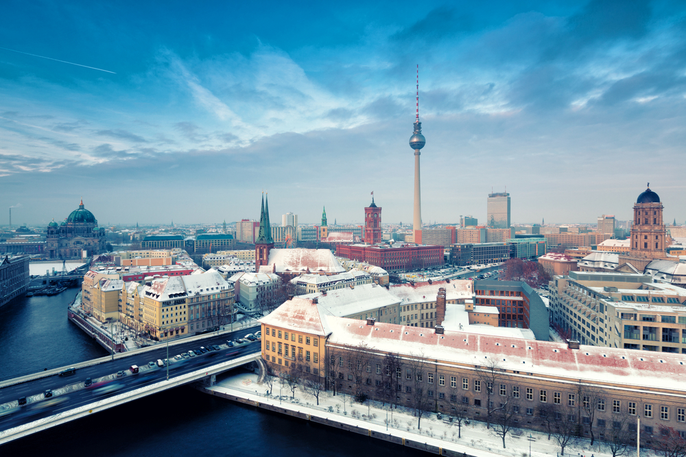 An aerial view of the Berlin cityscape in winter, with snow-covered rooftops and the iconic TV Tower.