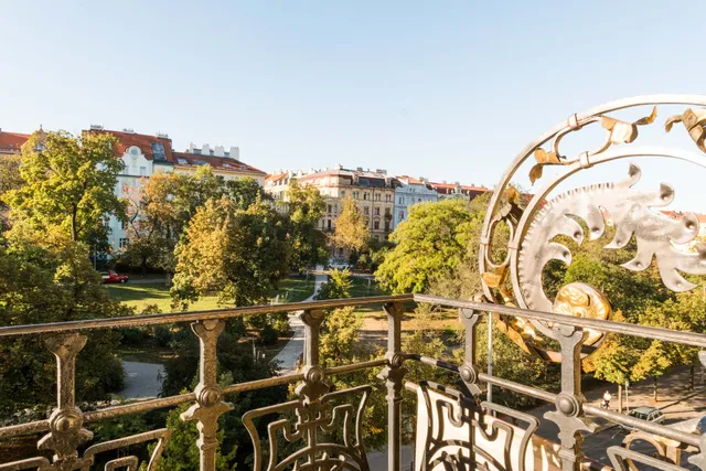 View from an ornate metal balcony overlooking a city park with buildings in the background.