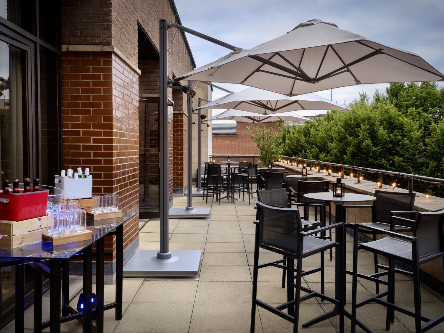 An outdoor terrace with tables, chairs, and large umbrellas next to a brick building.