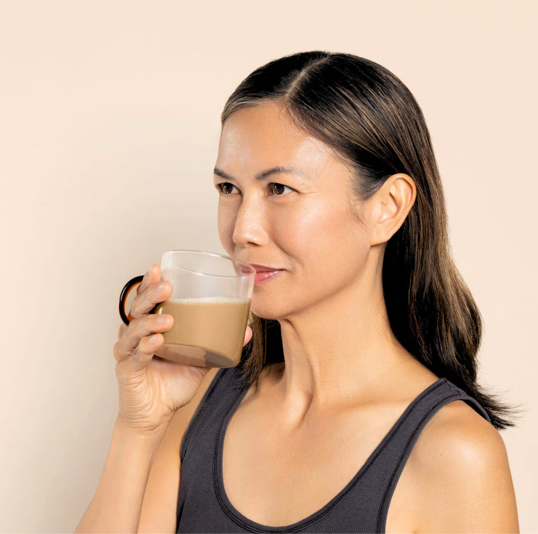 Person drinking a cup of coffee against a beige background.