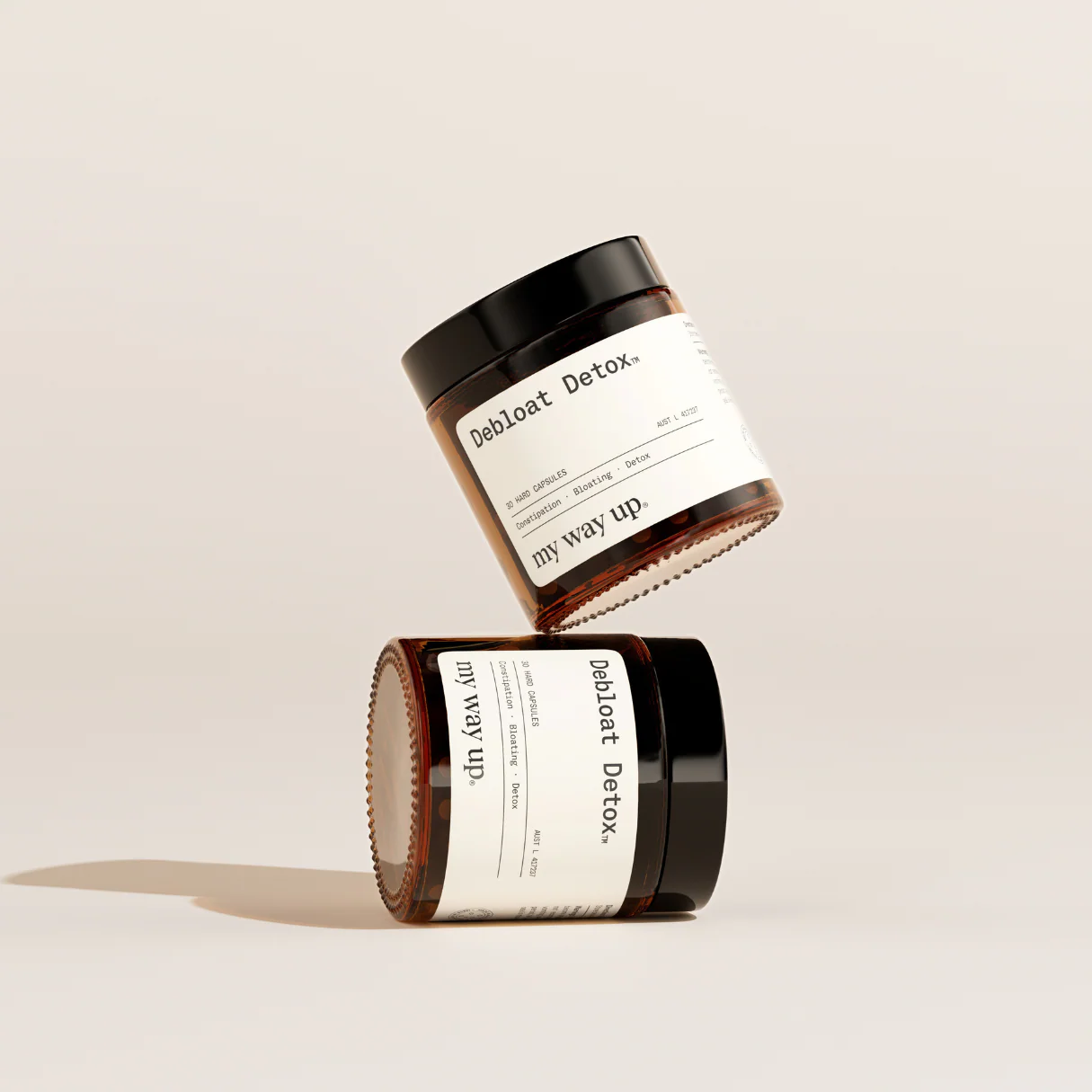 Two amber glass jars of Debloat Detox supplements, with one balanced on top of the other.