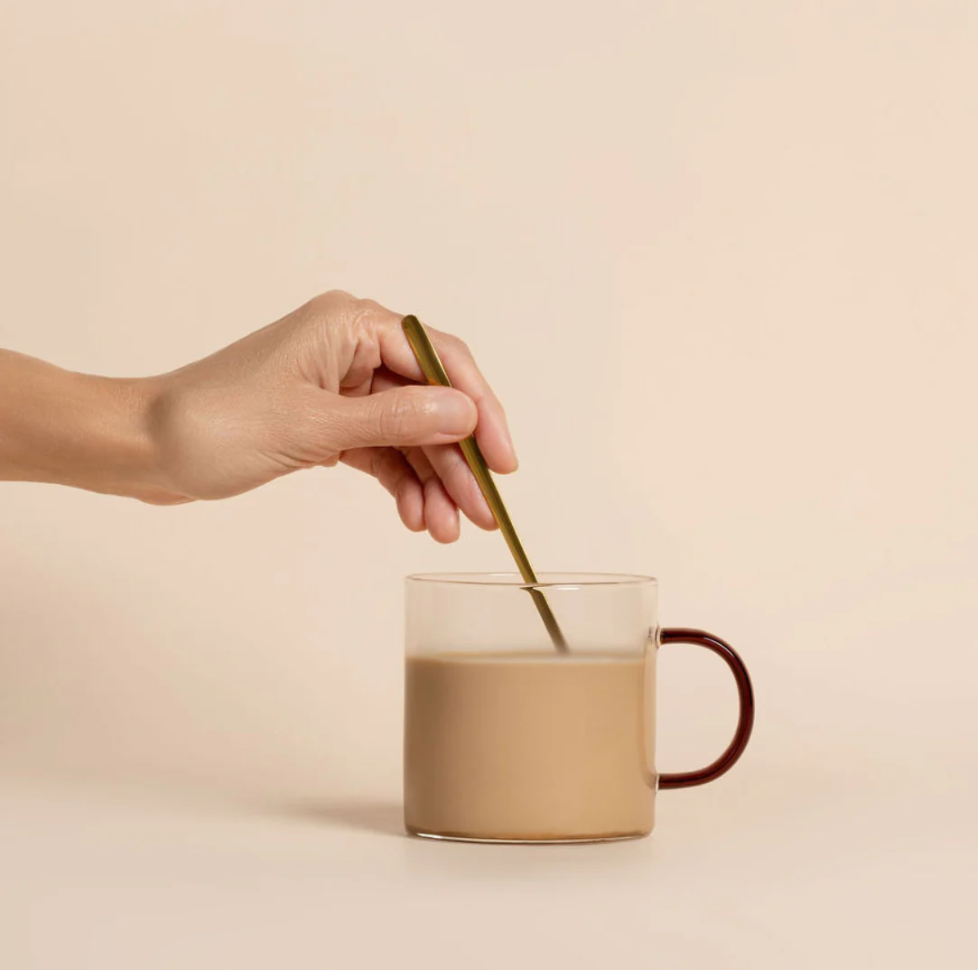 Hand stirring a cup of coffee with a spoon.