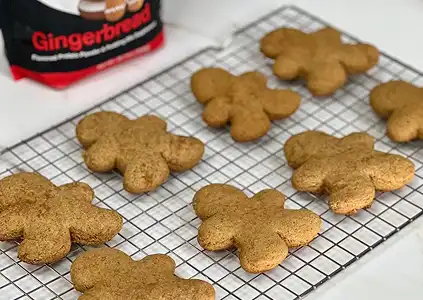 Plain gingerbread man cookies cooling on a wire rack with a bag of gingerbread mix behind them.