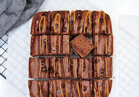 An overhead shot of sliced chocolate brownies drizzled with caramel and topped with chocolate chips.