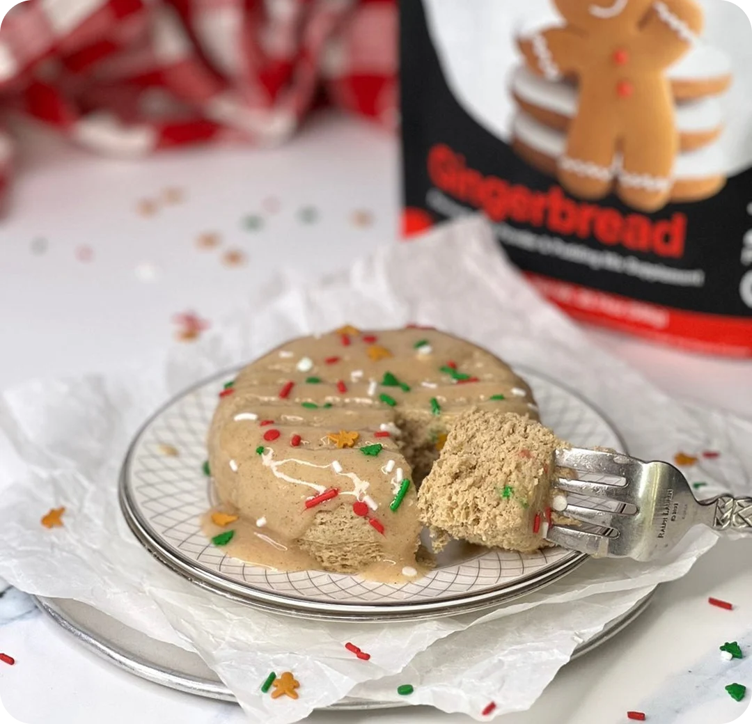 A fork takes a bite of a small gingerbread cake with glaze and festive sprinkles on a plate.