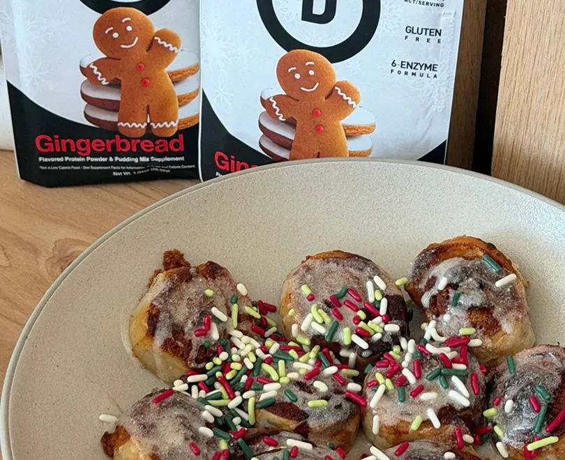 A plate of small iced pastries with sprinkles, with bags of gingerbread protein powder in the background.