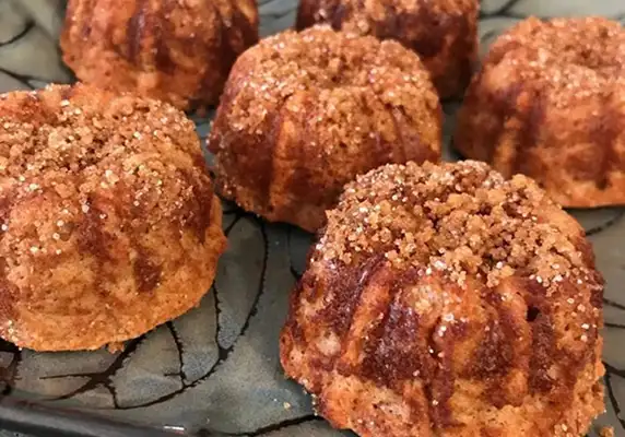 A close-up of several small, round cinnamon cakes with a crumble topping on a patterned plate.