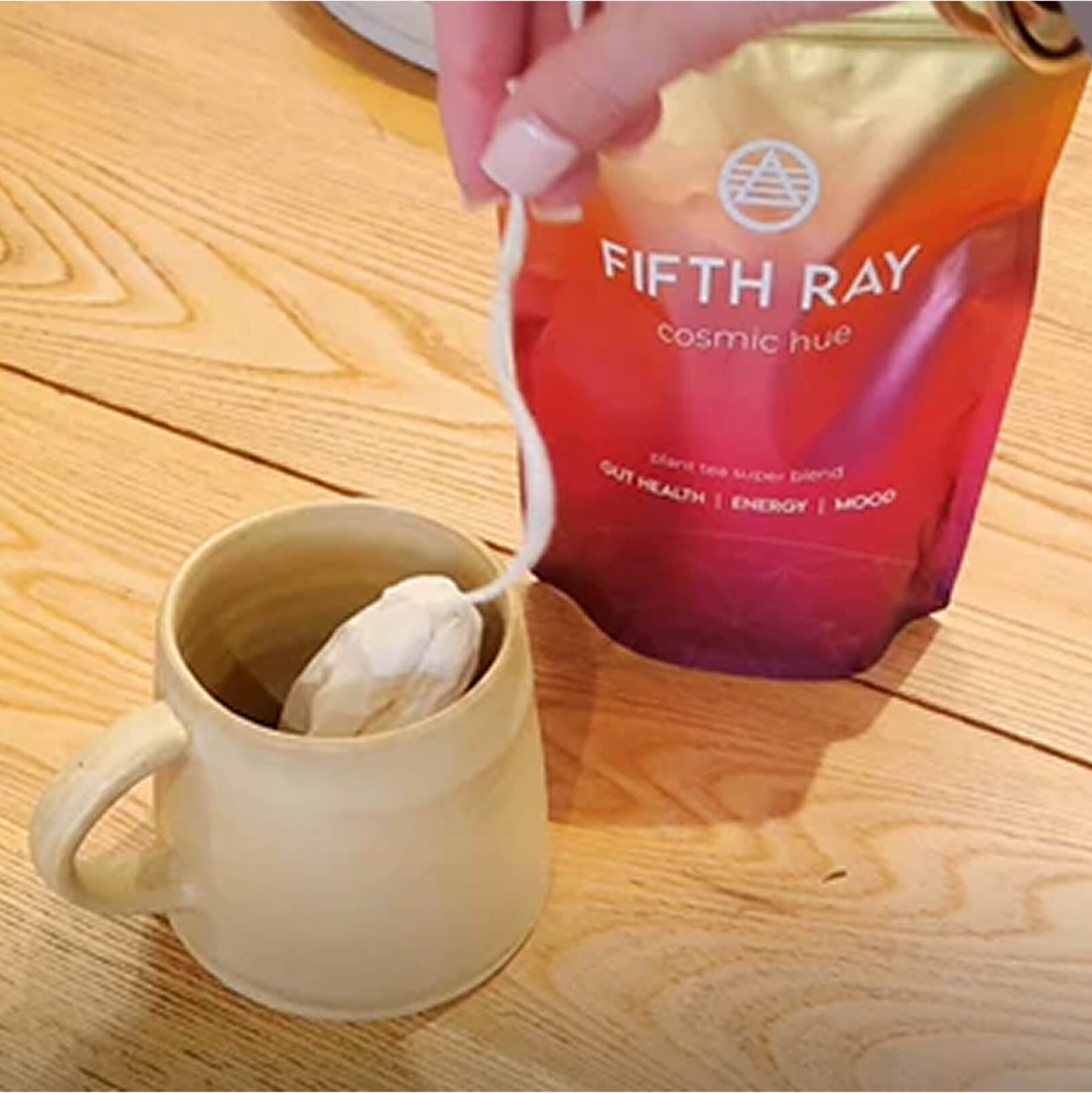 Hand placing a tea bag into a beige mug beside a colorful tea package.