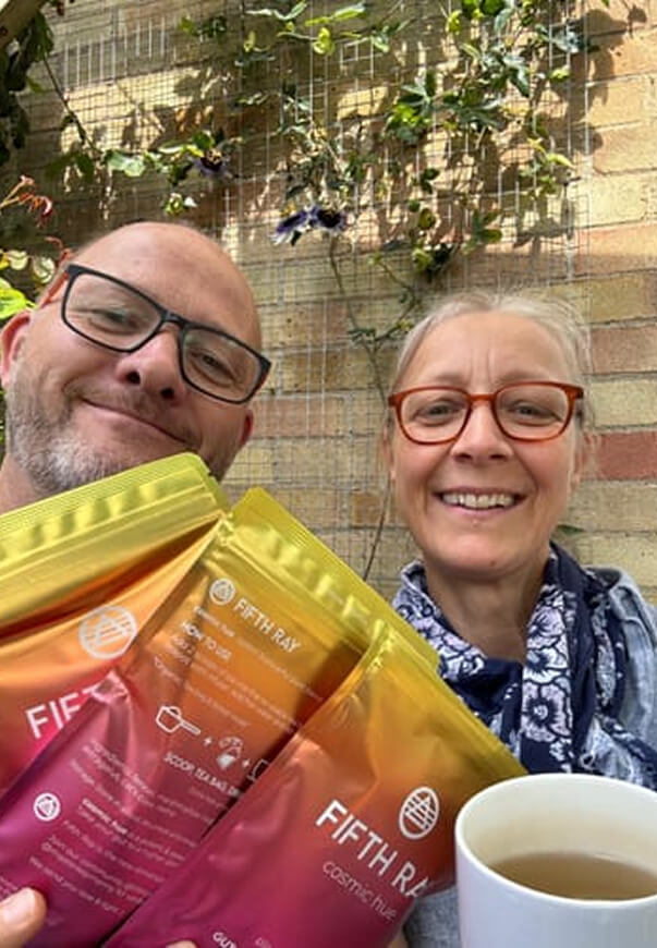 Two people smiling, holding Fifth Ray product packages and a cup of tea.