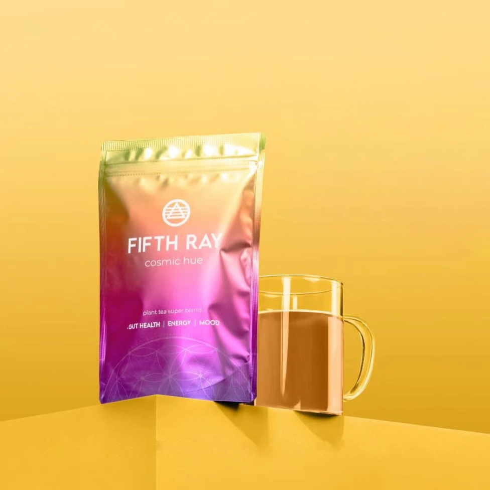 A colorful pouch of Fifth Ray cosmic hue plant tea next to a glass mug of the beverage.