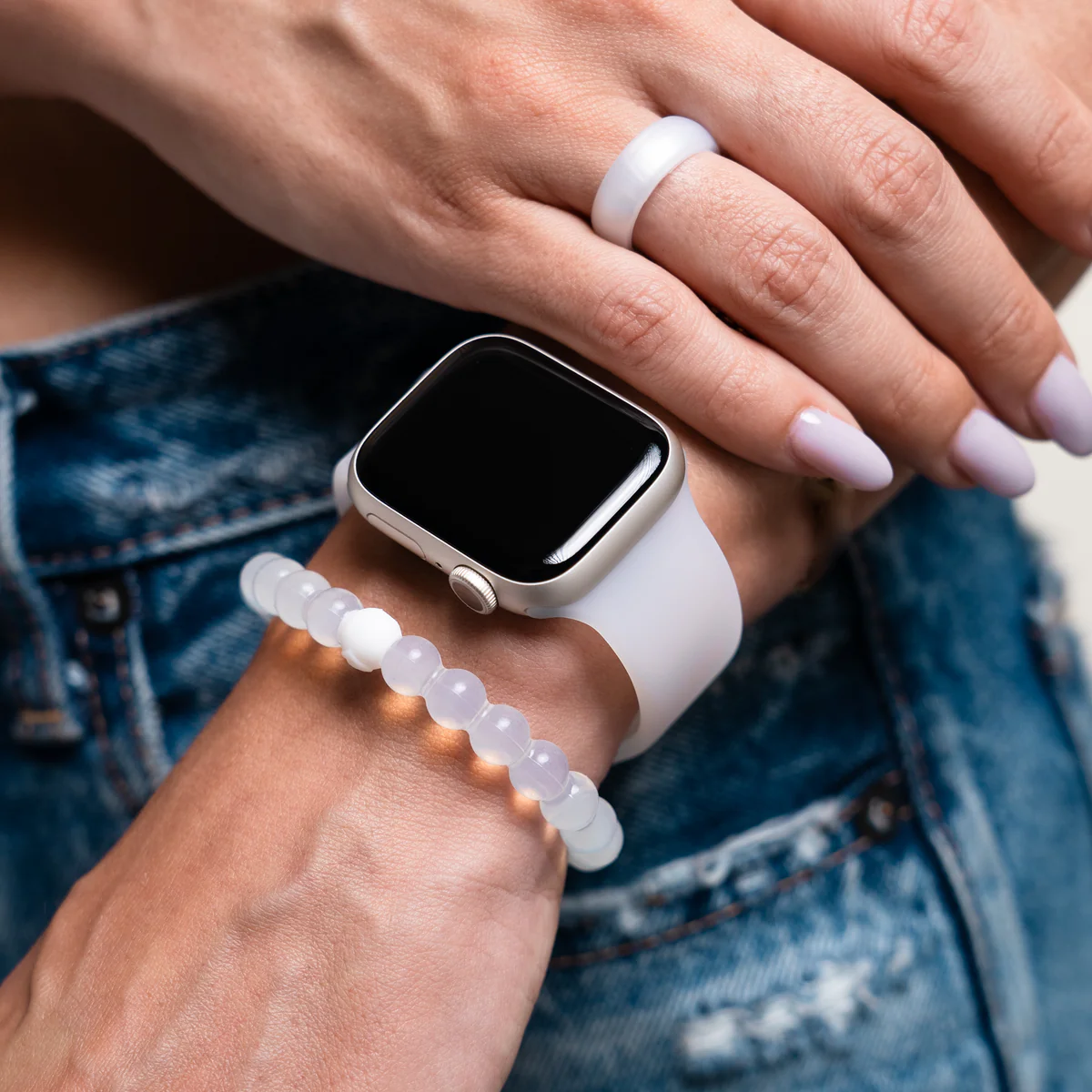 Person wearing a white watch, bracelet, and ring with denim clothes visible.