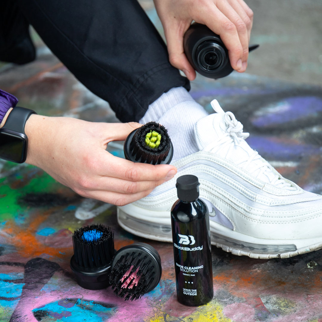 Person cleaning white sneakers with brushes and shoe cleaning solution.