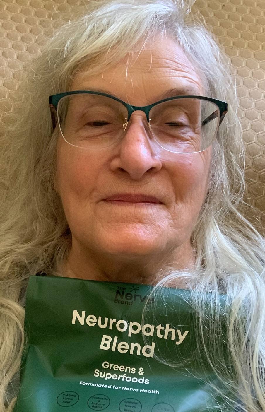 An older woman with glasses holds up a green pouch of Neuropathy Blend Greens & Superfoods.