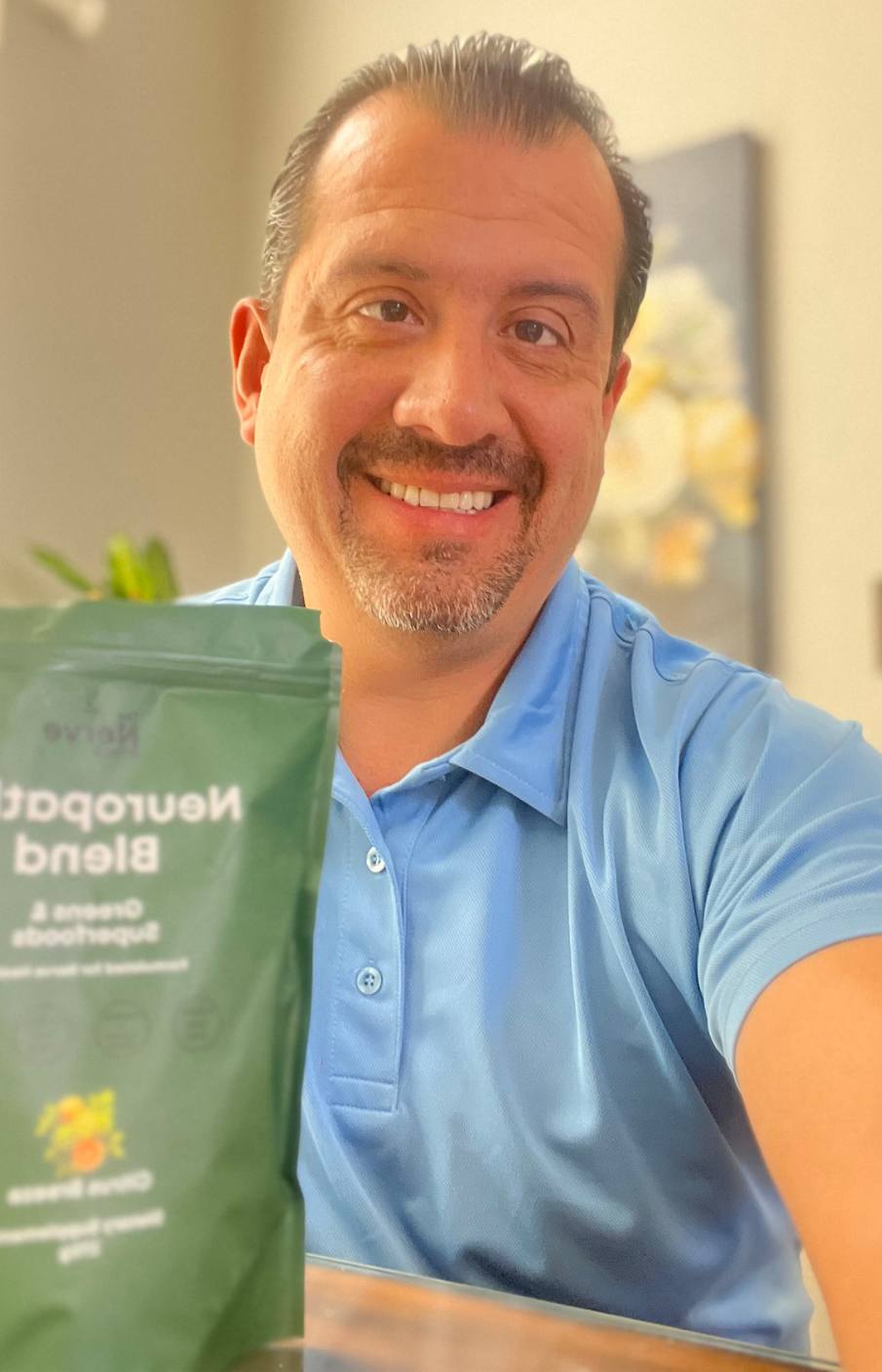A man in a light blue polo shirt smiles while holding a green pouch.