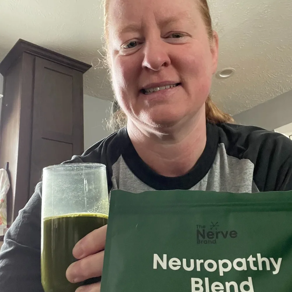 Person holding a glass with a green drink and a Neuropathy Blend package.