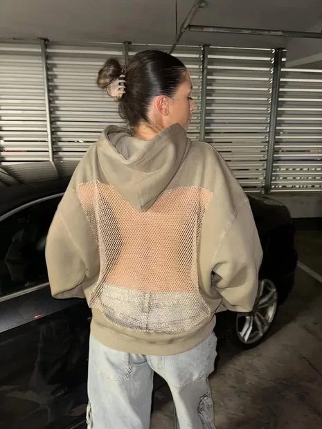 Person wearing a hoodie with a mesh back standing near a car in a garage.