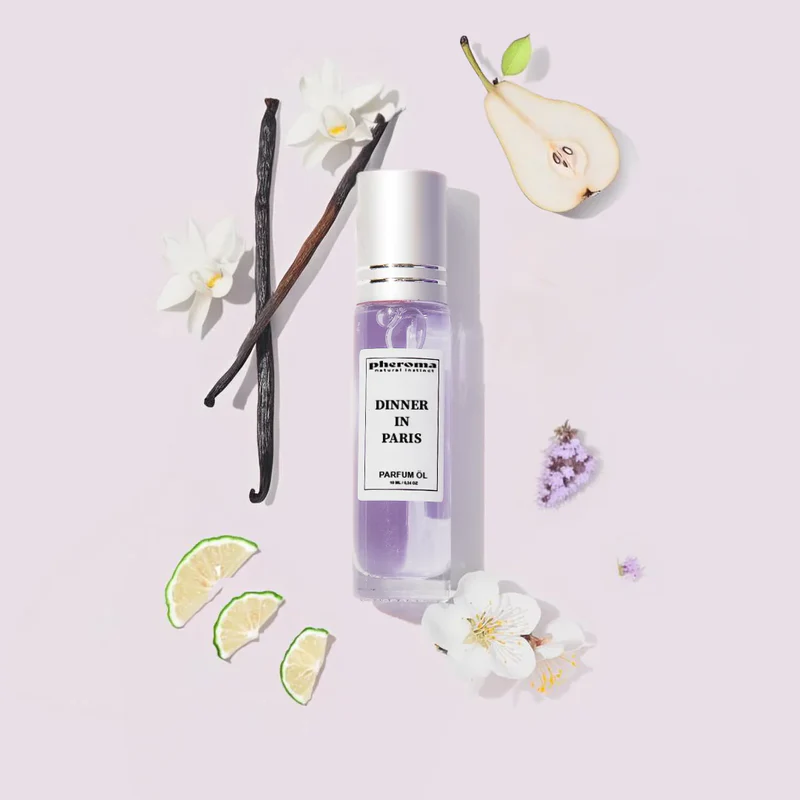 Perfume bottle with flowers, vanilla beans, pear slice, and lime wedges on a light background.