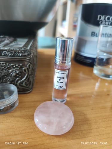 Perfume bottle labeled 'Dinner in Paris' beside a decorative box and pink stone on a wooden surface.